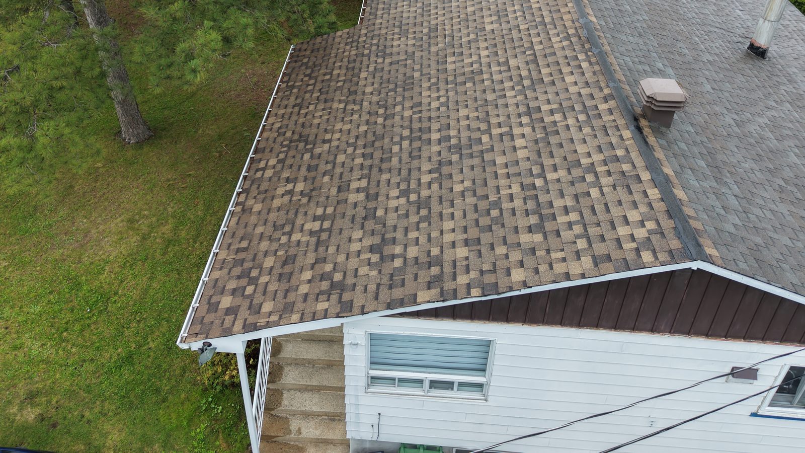 Drone view of an asphalt shingle bungalow roof surrounded by trees