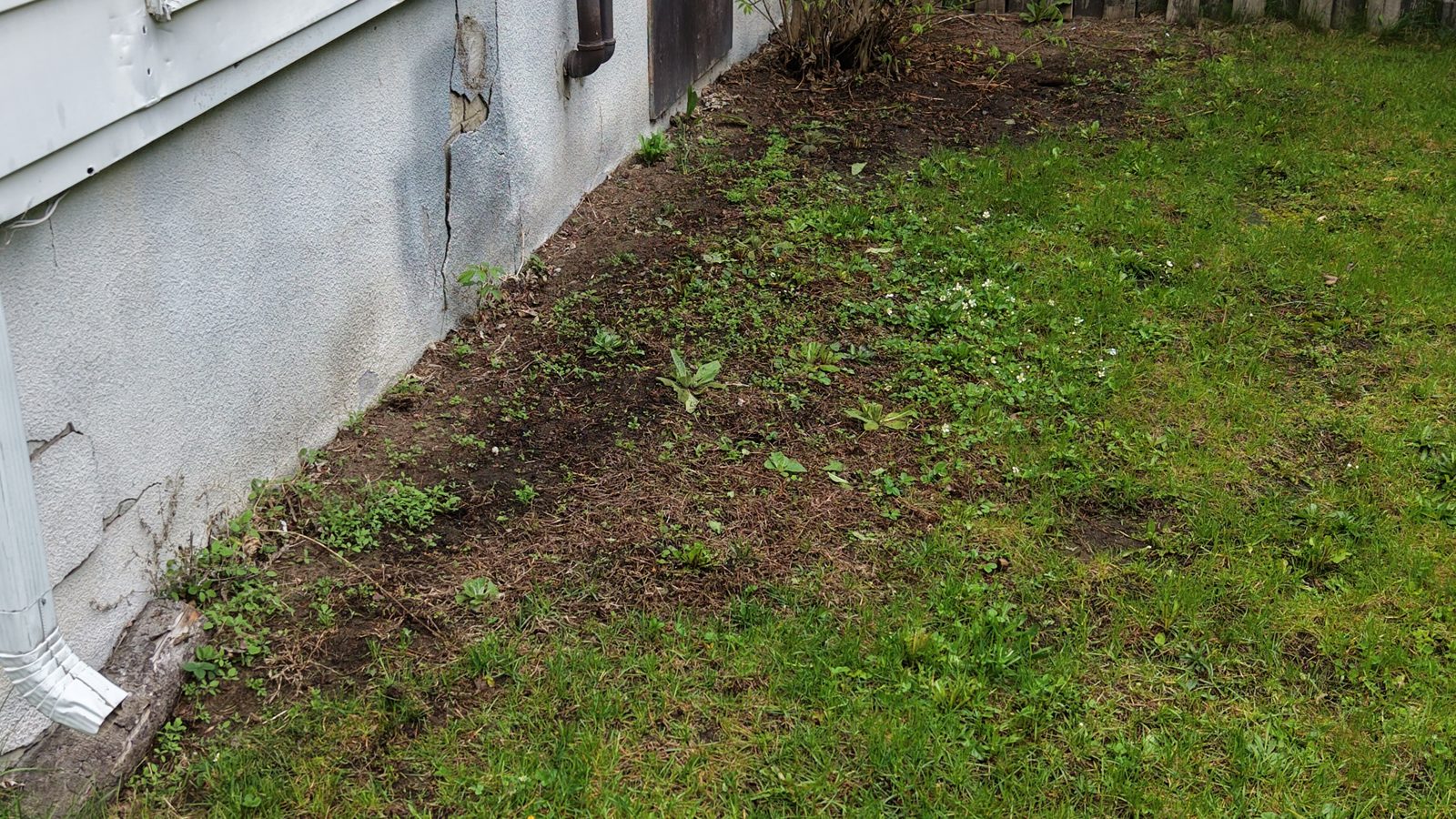 Cracked parging along a house foundation, with a downspout at the corner