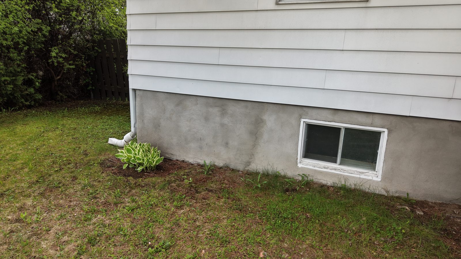 Bungalow foundation with a basement window and a downspout, seen during a home inspection