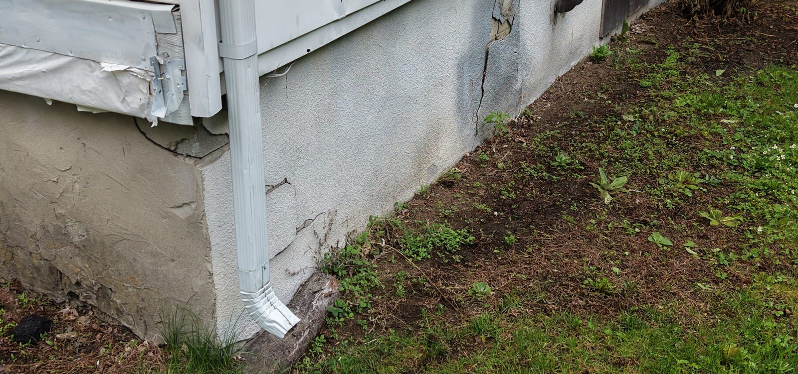 Fondation de maison avec crépi fissuré et descente de gouttière, photographiée lors d'une inspection à Montréal