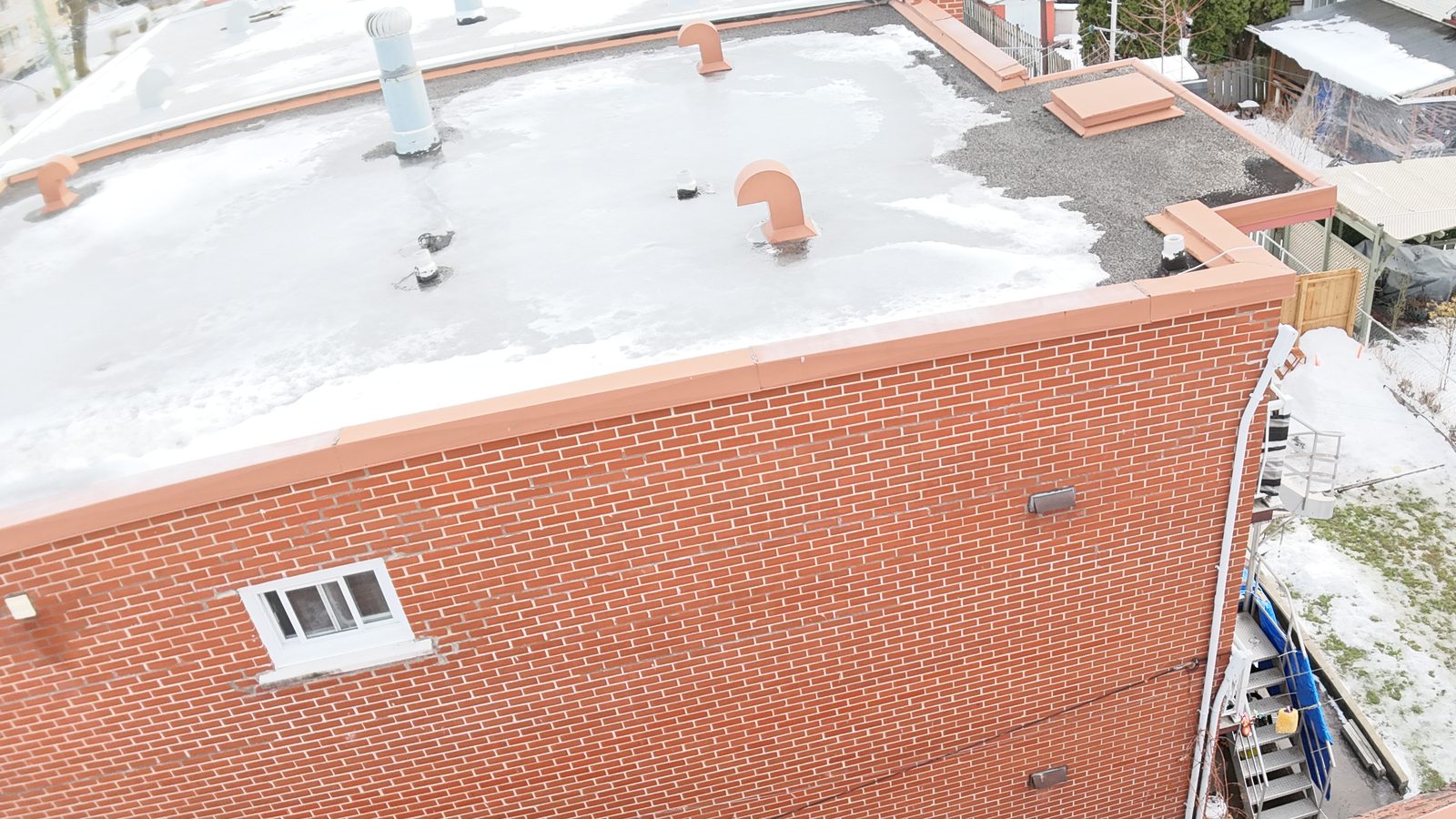 Brick plex with a flat roof and a cracked parapet coping, photographed by drone during an inspection