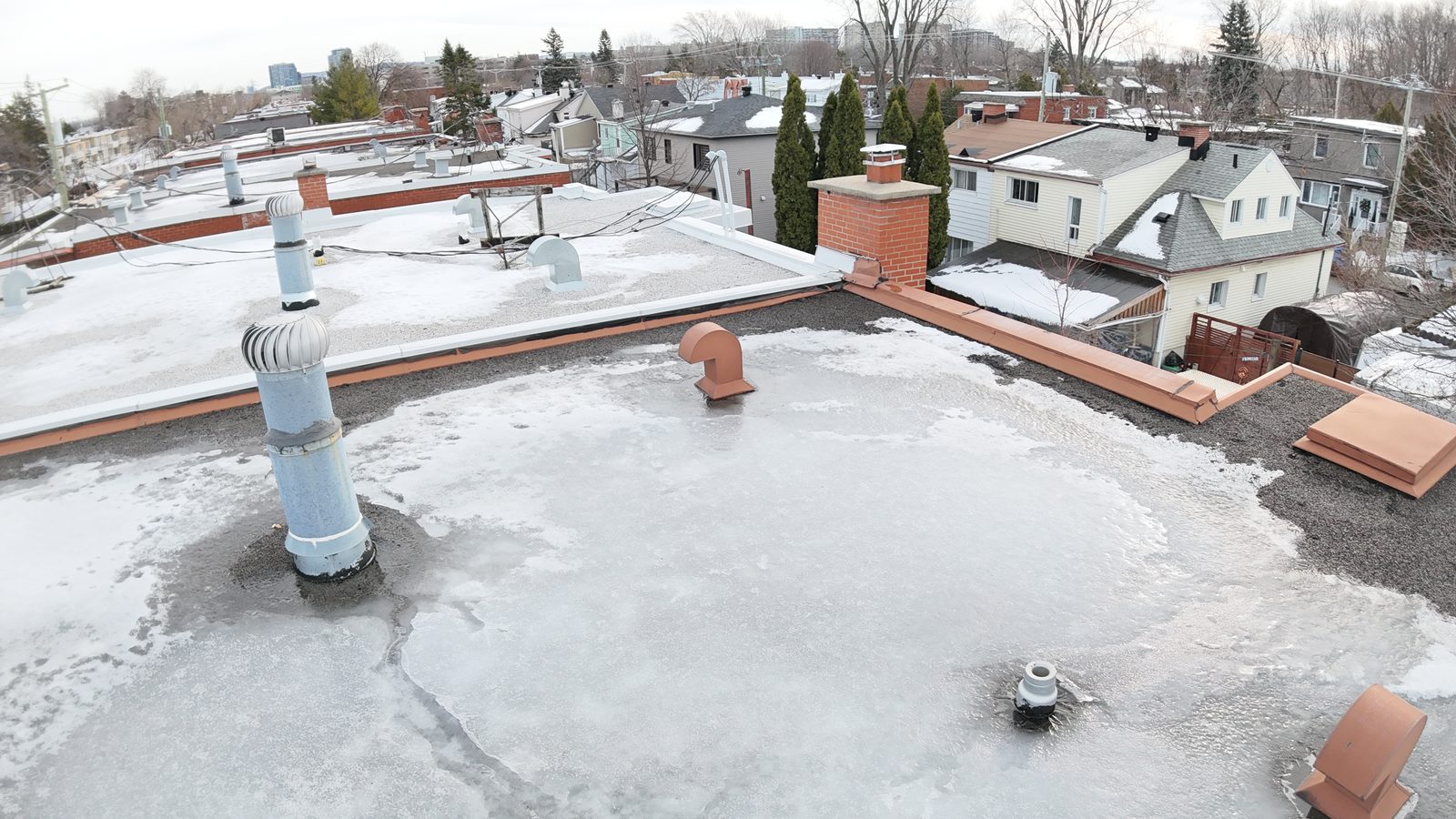 Flat roof of a plex with vents and a chimney in a residential street, photographed by drone during an inspection