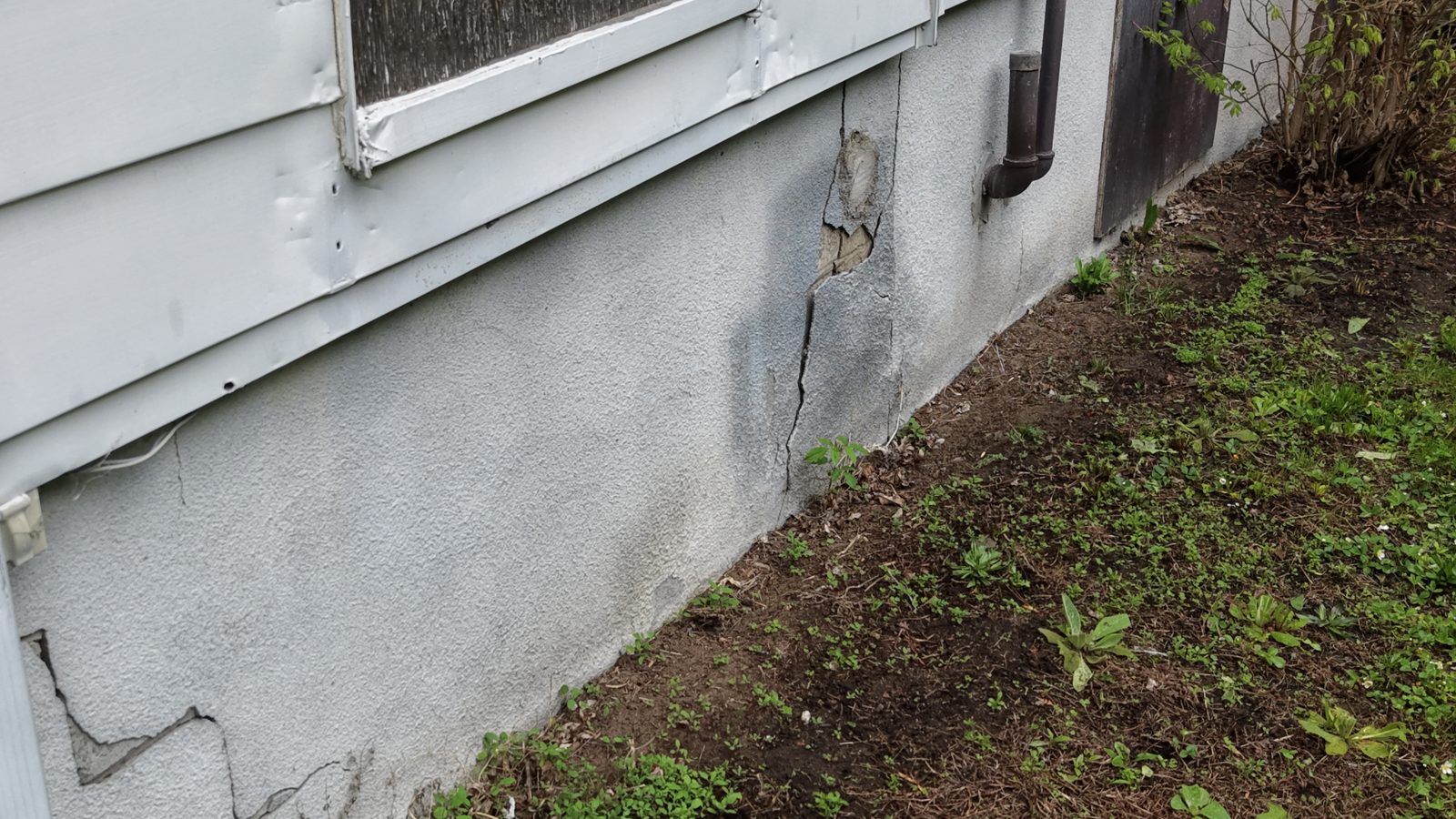 Cracked foundation parging below a basement window, a common way for water to reach a basement